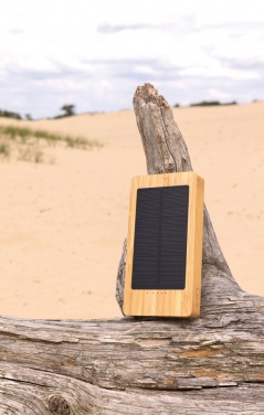 Pruun Sunwick 10 000 mAh bambusest päikeseakupank — kasutuspilt puidust pinnal, logoga personaliseeritav, Logo.ee