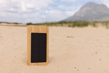 Pruun Sunwick 10 000 mAh bambusest päikeseakupank — püstine kasutuspilt liival, logoga personaliseeritav, Logo.ee